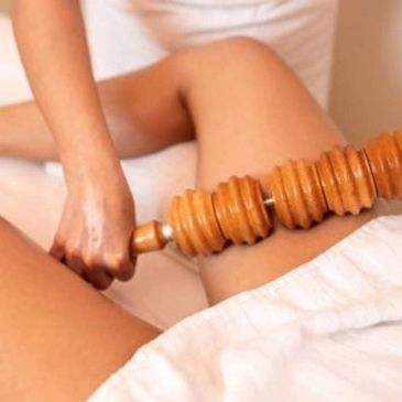 A person using a wooden roller massage tool on their thigh.