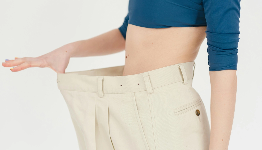 Person showing loose beige pants around waist.