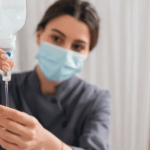 A nurse adjusting an IV drip wearing a face mask.