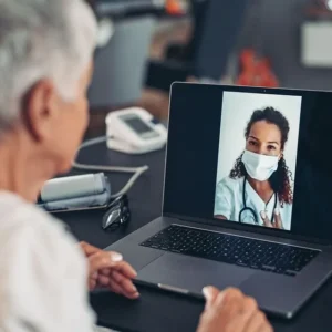 An elderly man video calling a female doctor wearing a face mask.