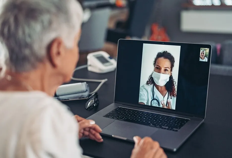 An elderly man video calling a female doctor wearing a face mask.