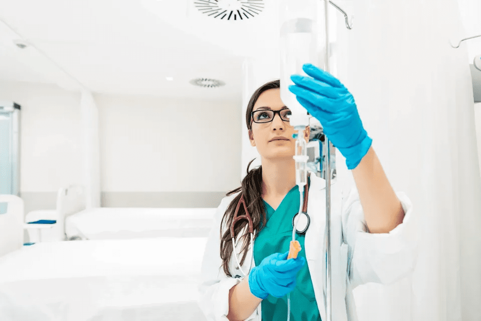 A female doctor examining an IV drip in a hospital room.