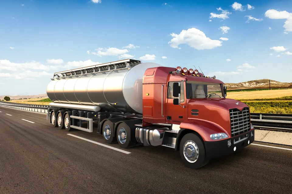 A red tanker truck driving on a highway under a blue sky.