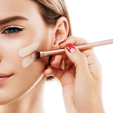 Applying makeup foundation on a woman's cheek with a brush.