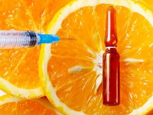 A syringe and medicine vial placed on sliced oranges.